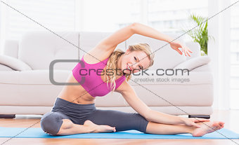 Fit blonde stretching on exercise mat smiling at camera