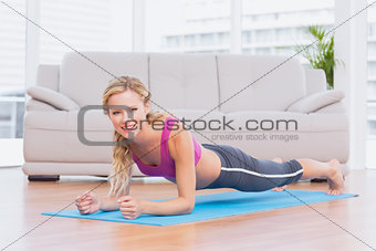 Fit blonde in plank position on exercise mat smiling at camera