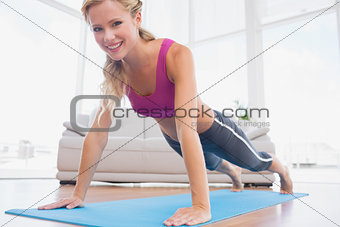 Strong blonde in plank position on exercise mat smiling at camera