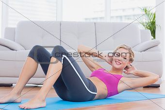 Slim blonde doing sit ups on exercise mat smiling at camera