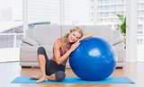 Toned blonde sitting beside exercise ball smiling at camera
