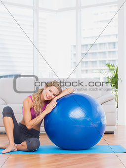 Fit blonde sitting beside exercise ball smiling at camera