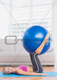 Smiling blonde holding exercise ball between legs