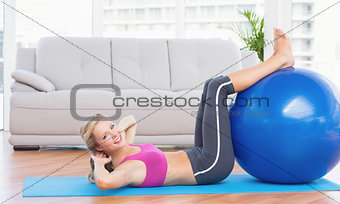 Cheerful fit blonde doing sit ups with exercise ball