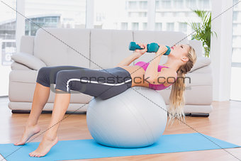 Smiling blonde doing sit ups with exercise ball holding dumbbells