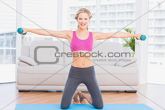 Happy blonde lifting dumbbells on exercise mat