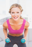 Fit blonde lifting dumbbells and smiling at camera