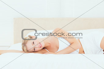 Pretty blonde lying on her bed smiling at camera