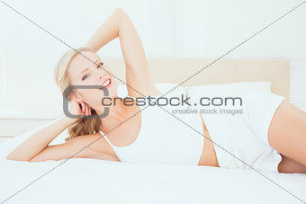 Sexy young blonde lying on her bed smiling at camera
