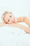 Cheerful young blonde lying on her bed smiling at camera