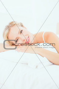 Cheerful young blonde lying on her bed smiling at camera