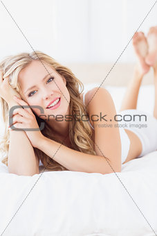 Cheerful young blonde lying on her bed looking at camera