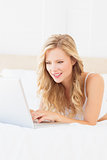 Cheerful young blonde lying on her bed using laptop