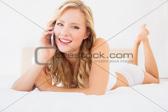 Young blonde on the phone lying on bed smiling at camera