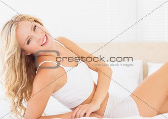 Attractive blonde woman lying on bed smiling at camera