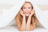 Attractive blonde smiling at camera from under the duvet