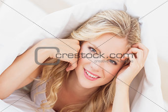 Sexy young blonde smiling at camera from under the sheet