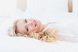 Sexy young woman in white shirt smiling at camera lying on bed