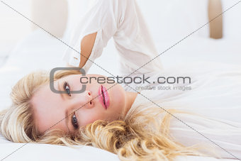 Beautiful young woman in white shirt smiling at camera lying on bed