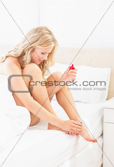 Pretty young blonde painting her toenails at edge of bed