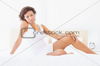 Pretty brunette sitting on bed smiling at camera