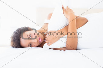 Smiling brunette lying on bed hugging pillow