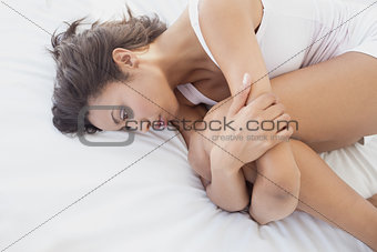 Unhappy brunette lying on bed holding her knees