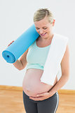 Pregnant blonde smiling at bump holding exercise mat
