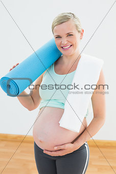 Pregnant woman smiling at camera holding exercise mat