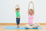 Pregnant smiling mother and daughter doing yoga together