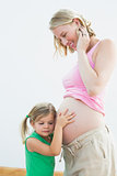 Little girl listening to blonde mothers pregnant belly