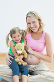 Pregnant woman smiling at camera with her young daughter