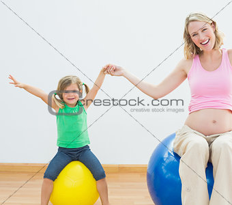 Happy pregnant woman bouncing on exercise ball with young daughter