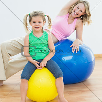 Smiling pregnant woman exercising on exercise ball with young daughter