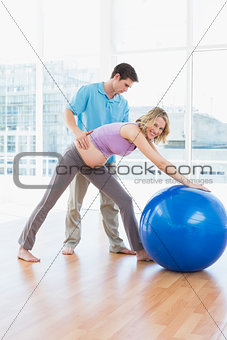 Cheerful pregnant woman exercising with trainer and ball