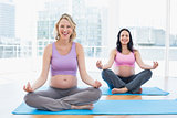 Smiling pregnant women in yoga class in lotus pose