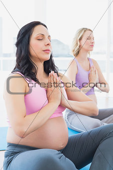 Meditating pregnant women at yoga class sitting with hands together