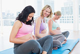 Smiling pregnant women sitting in yoga class touching their bumps