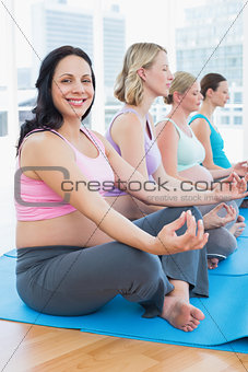 Content pregnant women meditating in yoga class with one smiling at camera