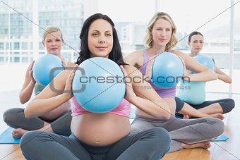 Happy pregnant women in yoga class holding medicine balls