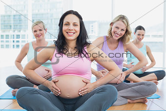 Happy pregnant women in yoga class holding their bumps