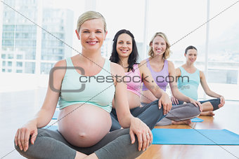 Happy pregnant women in yoga class sitting on mats
