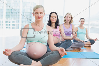 Pregnant women in yoga class sitting on mats with eyes closed