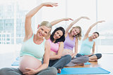 Pregnant women in yoga class sitting on mats stretching arms
