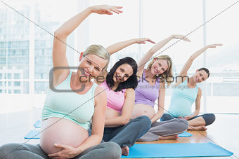 Pregnant women in yoga class sitting on mats stretching arms