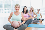 Pregnant women in yoga class sitting on mats touching their bumps