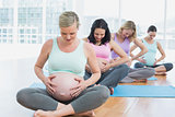 Pregnant women sitting on mats touching their bumps