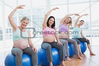 Pregnant women sitting on exercise balls stretching arms