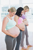 Cheerful pregnant women standing in a line smiling at bumps
