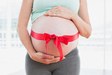Pregnant woman standing with red bow around bump